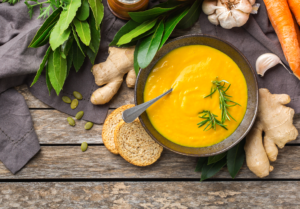 Creamy fall soup surrounded by carrots and ginger on a wooden counter top