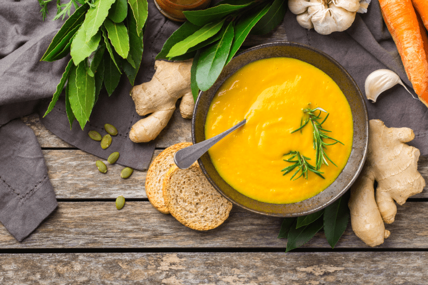 Creamy fall soup surrounded by carrots and ginger on a wooden counter top