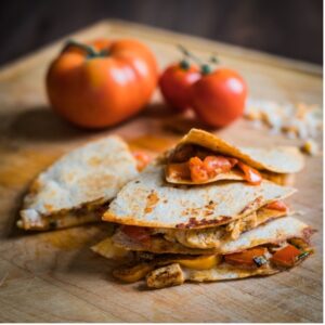 Grilled chicken quesadillas chopped into slices with fresh tomato on a cutting board