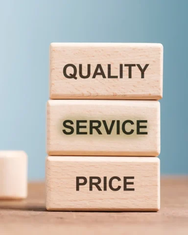 Three stacked wooden blocks labeled ‘QUALITY,’ ‘SERVICE,’ and ‘PRICE,’ with ‘QUALITY’ at the top, against a neutral blue background.