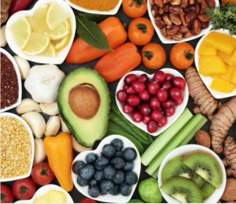 Assortment of colourful fruits, vegetables, nuts, and spices arranged in bowls and on a flat surface.