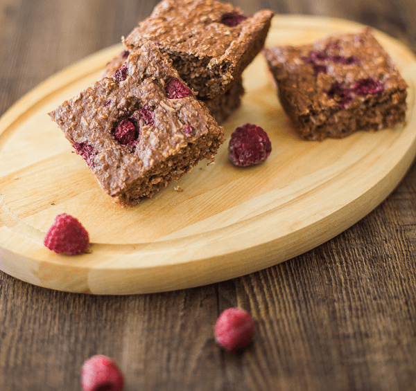 Baked chocolate raspberry oatmeal bars stacked on a wooden board with fresh raspberries.