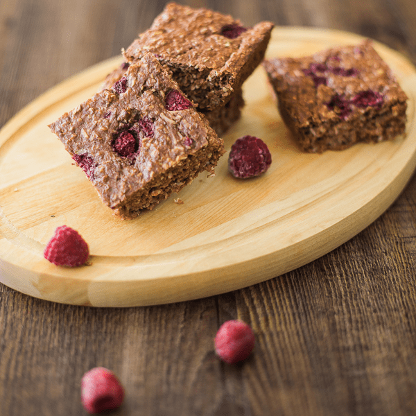 Baked chocolate raspberry oatmeal bars stacked on a wooden board with fresh raspberries.